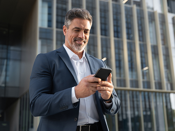 Mature business man outside office building looking at mobile phone.