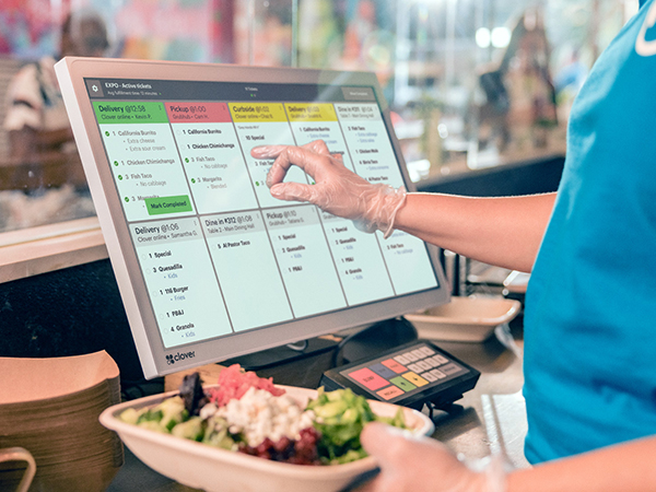 Person in the kitchen of a restaurant looking at the orders coming in on a screen.