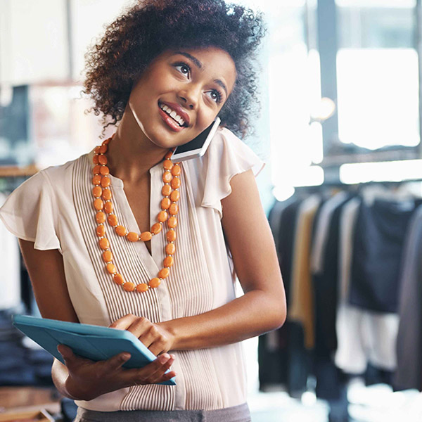 Female business owner talking on a phone while holding a tablet in her clothing store.
