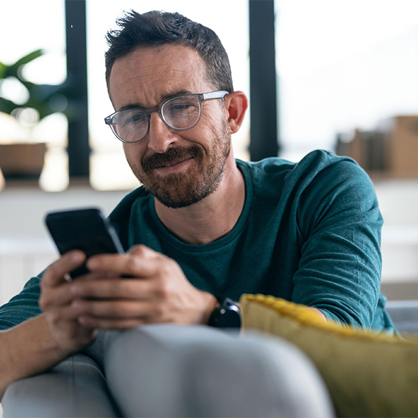 Man sitting on couch looking at phone monitoring credit card spending