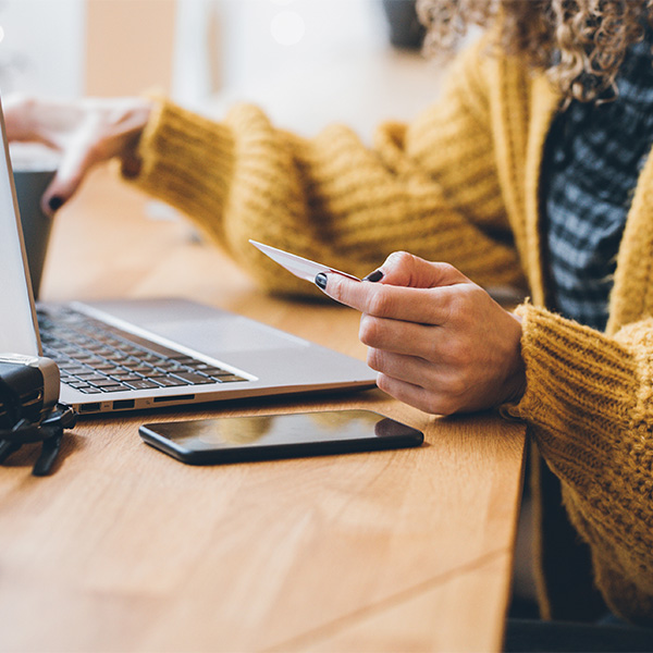 Women holding credit card while looking at her computer that is sitting on table.