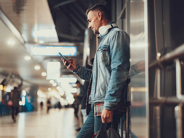 Man standing in airport looking down at phone.